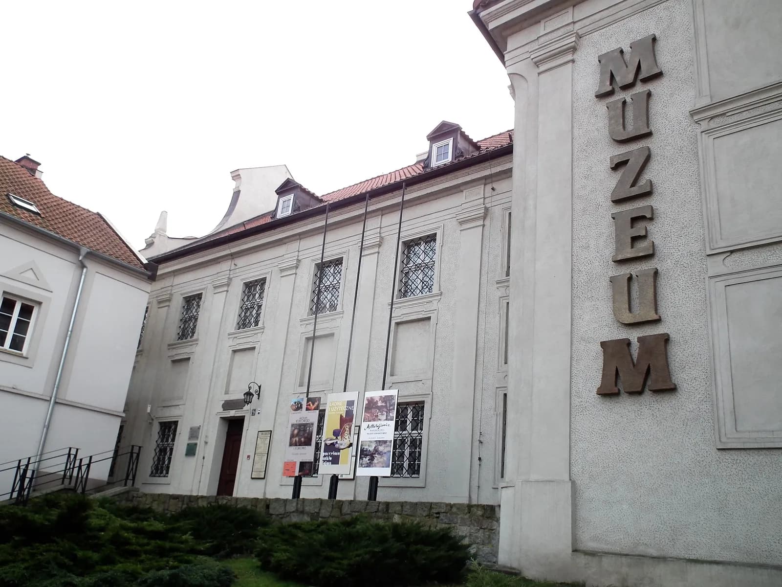An outdoor shot of a historical building with the word "MUZEUM" written vertically on its right face, and various posters hanging on the front.